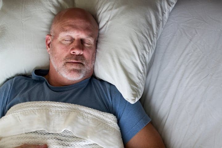 A man sleeping soundly in bed under soft light.