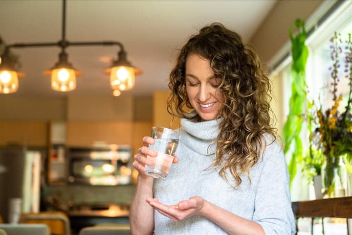 A woman holding two supplement capsules up to the light.